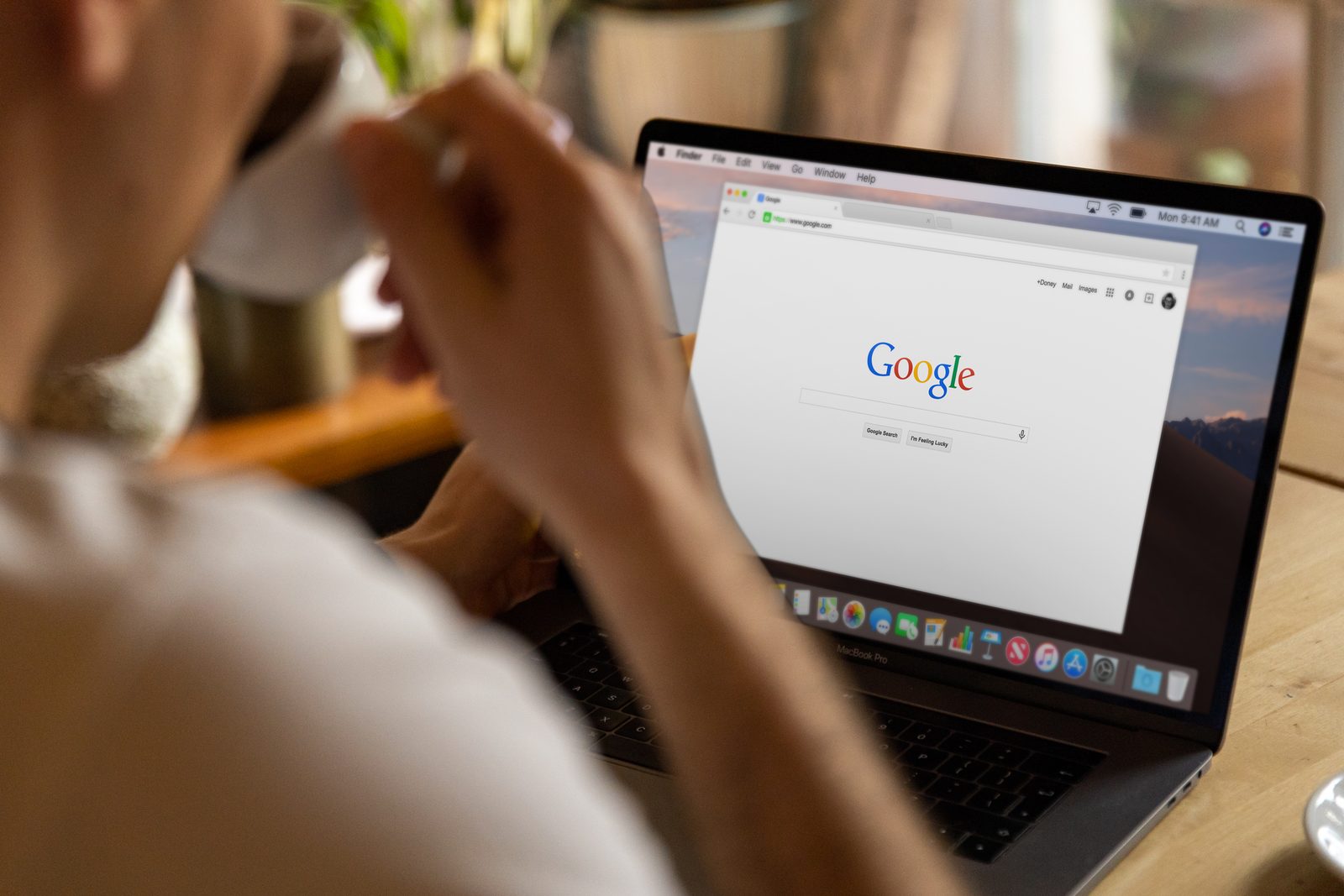 A person drinking coffee at a laptop with the Google homepage open on screen