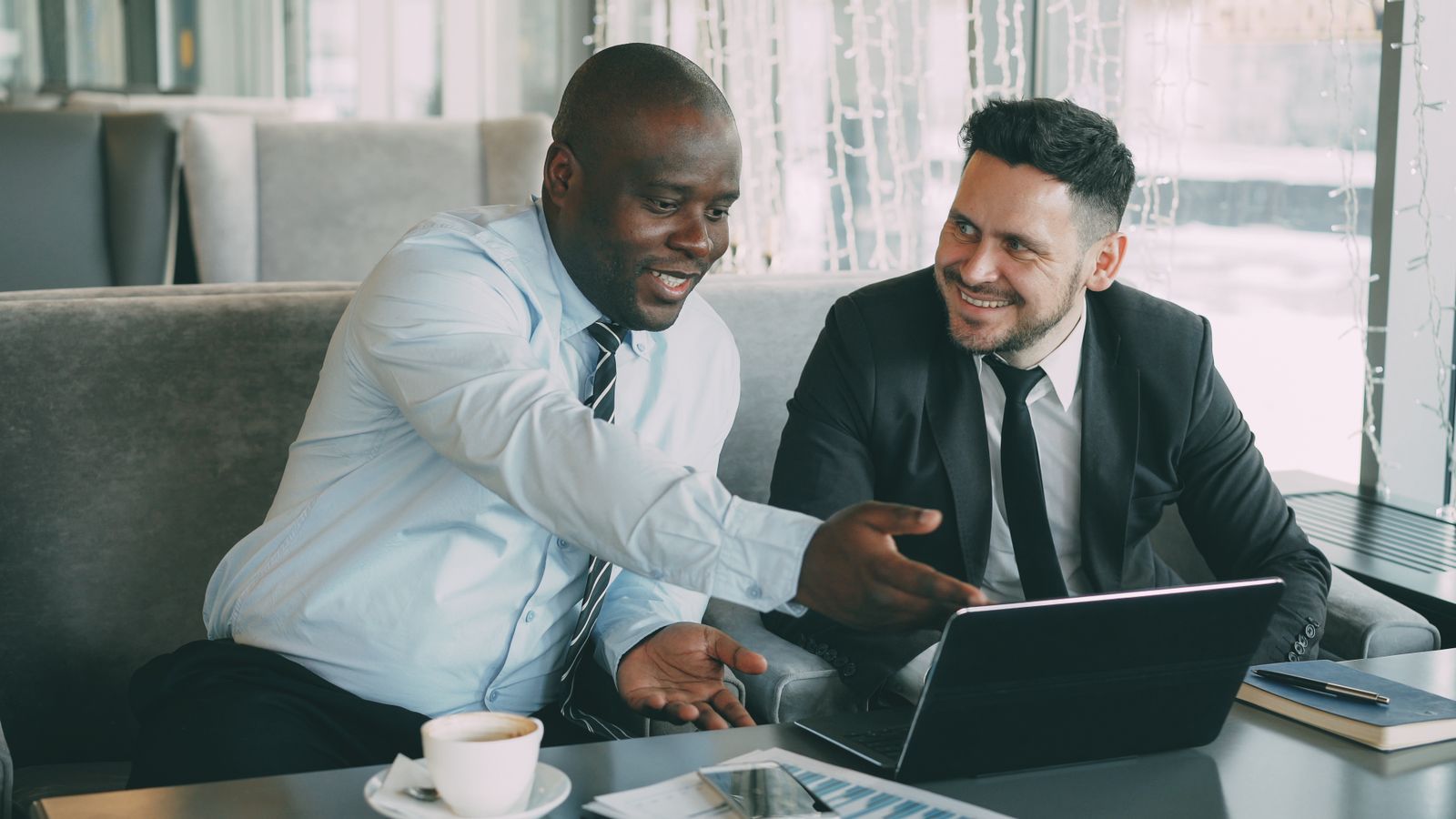 Two business professionals smiling as they look at a laptop together over coffee in a modern office