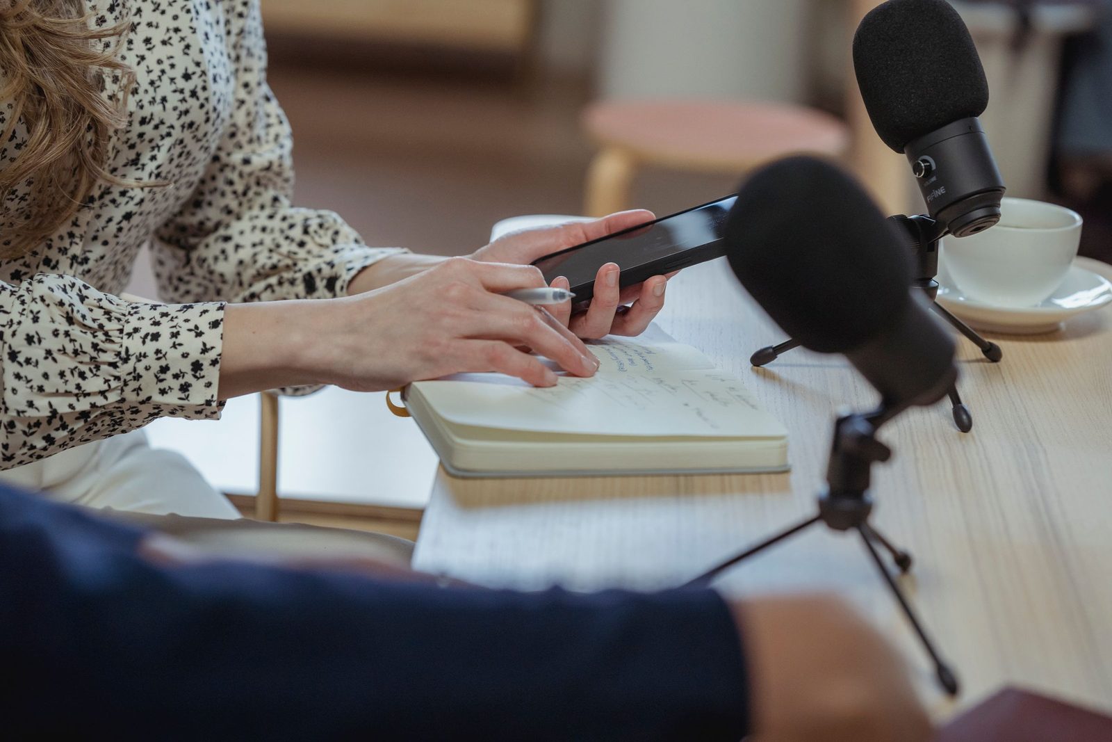 A journalist taking notes beside a microphone and a phone recorder during an interview